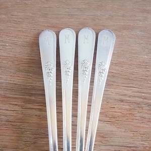 May include: Four silver-plated teaspoons with an ornate floral design and the letter "M" engraved on the handle.
