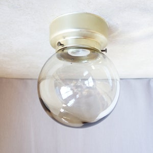 May include: A ceiling light fixture with a round, smoked glass shade and a gold metal base.