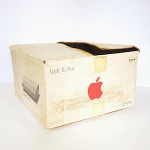 May include: A rectangular, off-white cardboard shipping box for an Apple IIc Plus computer. The box features a red Apple logo, the text Apple IIc Plus, a graphic illustration of the computer, and the model number A2S4500 printed on the side.