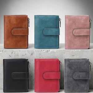 Può includere: Sei portafogli in pelle di vari colori: marrone, verde acqua, rosa, nero, rosso e grigio. Ogni portafoglio ha una chiusura con cerniera e una patta frontale con bottone a pressione. I portafogli sono esposti su una superficie multilivello.
