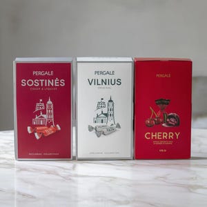Puede incluir: Tres cajas de bombones Pergale. Las cajas son rojas y blancas con texto e ilustraciones. Las cajas rojas dicen "SOSTINĖS" y "CHERRY". La caja blanca dice "VILNIUS". Las cajas están sobre una superficie de mármol.
