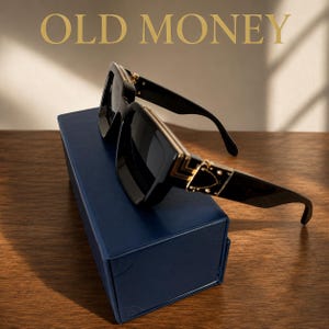 Könnte beinhalten: Schwarze Sonnenbrille mit dunklen Gläsern und goldfarbenen Metallakzenten an den Bügeln, platziert auf einer rechteckigen marineblauen Schachtel. Der Text OLD MONEY steht in goldener Schrift über der Sonnenbrille mit dickem Rahmen.