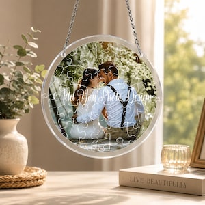 May include: A clear, circular puzzle with a photo of a couple, hanging by a silver chain. The puzzle has the text "Add Your Photo Design". The background includes a vase with greenery, a candle holder, and a book.