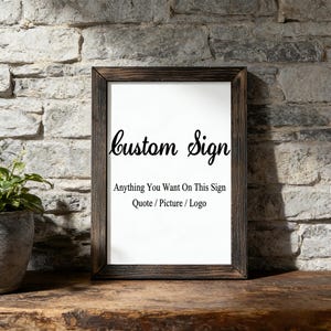 May include: A rectangular sign in a dark brown wooden frame with a white background. The text reads "custom Sign" in a black script font, followed by "Anything You Want On This Sign" and "Quote / Picture / Logo" in a black sans-serif font.