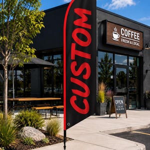 May include: A tall, black feather flag with a red border and the word CUSTOM printed in large, bold red letters. The flag is mounted on a silver metal cross-base stand, positioned upright on a concrete sidewalk outside a commercial building.