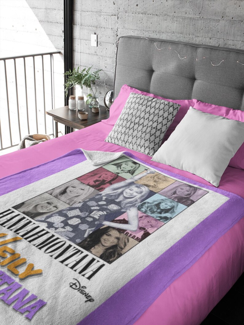 Pu&ograve; includere: Una coperta bianca e viola con un collage di immagini di Hannah Montana. La coperta ha un bordo viola ed &egrave; esposta su un letto con lenzuola e cuscini rosa. Il logo Disney &egrave; visibile.