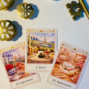 May include: Three tarot cards featuring illustrations of Paris and business themes, labelled 43. Opportunité, 2. Succès, and 26. Augmentation. The cards are surrounded by three gold-toned metal flower-shaped ornaments, a gold key, and a small white heart-shaped box.
