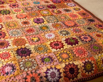 May include: A handmade, colorful crochet blanket. The blanket features a patchwork design with square motifs in shades of orange, pink, yellow, green, and purple. The edges are finished with a dark brown border.