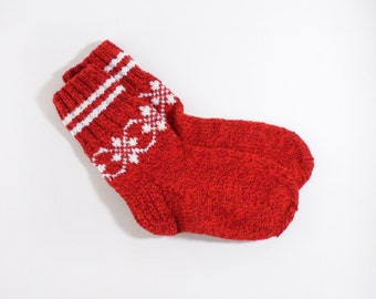 May include: A red knitted sock with white accents. The sock features a white floral design and two white stripes at the top. The sock is made of a thick, textured yarn.