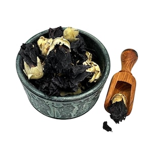 Può includere: Una ciotola di ceramica verde scuro piena di fiori di ibisco secchi rosso scuro e boccioli color beige chiaro. Un piccolo cucchiaio di legno contiene altri fiori secchi. La ciotola ha un design in rilievo dettagliato.