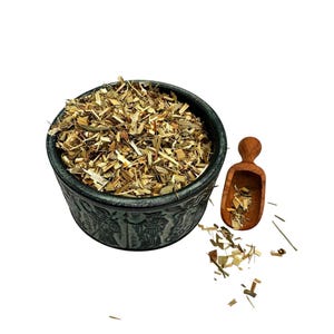 May include: A dark grey ceramic bowl with embossed figures on the exterior, filled with a mixture of dried tan and brown herbal plant pieces. A small wooden scoop containing a portion of the same dried herbs rests beside the bowl.