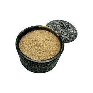 以下が含まれることがあります： 細かい薄茶色の粉末が入った、暗い色調の丸い容器。容器には人物や模様の複雑なレリーフ彫刻が施されています。ギリシャ風の精巧な彫刻が施されたお揃いの円形の蓋が、開いた容器の横に置かれています。