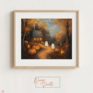 以下が含まれることがあります： 秋の森の中のコテージを描いた額装されたウォールアートプリント。小道には2体の小さな白い幽霊がおり、オレンジ色のカボチャ、光るランタン、浮かぶ金色の光に囲まれています。明るい木製のフレームに入っています。