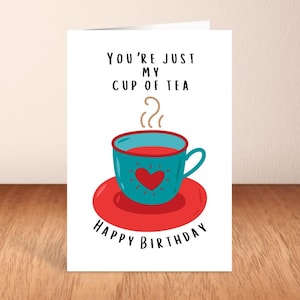 May include: A birthday greeting card with the text "You're just my cup of tea" and "Happy Birthday". The card features a teal teacup with a red heart on a red saucer. Steam rises from the cup.