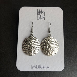 Puede incluir: Pendientes de c&iacute;rculo martillados de plata con una superficie texturizada. Los pendientes est&aacute;n en una tarjeta blanca con el texto "Libby Edith" y "LibbyEdith.etsy.com".