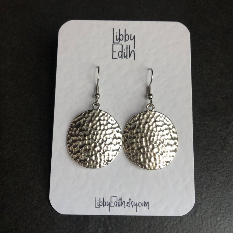 Puede incluir: Pendientes de c&iacute;rculo martillados de plata con una superficie texturizada. Los pendientes est&aacute;n en una tarjeta blanca con el texto "Libby Edith" y "LibbyEdith.etsy.com".