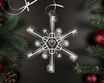 Könnte beinhalten: Ein weißer, schneeflockenförmiger Weihnachtsbaumschmuck mit einem Schlüssellochdesign und einem Herz mit einer Krone in der Mitte. Der Schmuck ist von Kiefernästen und roten Kugeln umgeben.