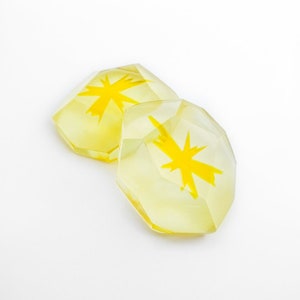 Puede incluir: Dos posavasos de resina amarilla con un diseño de estrella amarilla.