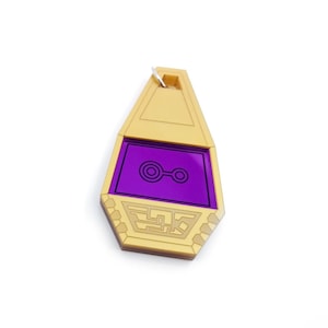 May include: A gold-colored pendant with a purple, translucent center featuring a stylized symbol. The pendant is shaped like a teardrop and has a small loop at the top for attaching a chain.