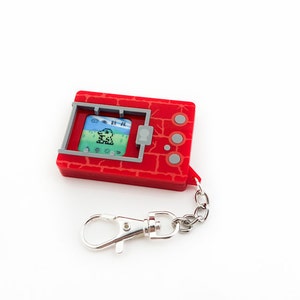 May include: Red and grey digital pet keychain with a small screen displaying a pixelated green creature. The keychain has a silver chain and a silver clasp.