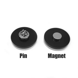 Pode incluir: Dois acess&oacute;rios redondos, pretos e prateados, um alfinete e o outro um &iacute;man. O alfinete tem um verso prateado. O &iacute;man tem um disco prateado no centro. As palavras "Pin" e "Magnet" s&atilde;o impressas abaixo.