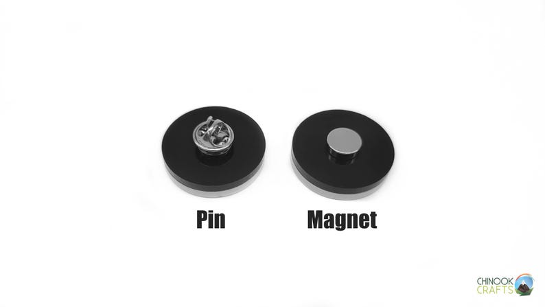 Pode incluir: Dois acess&oacute;rios redondos, pretos e prateados, um alfinete e o outro um &iacute;man. O alfinete tem um verso prateado. O &iacute;man tem um disco prateado no centro. As palavras "Pin" e "Magnet" s&atilde;o impressas abaixo.