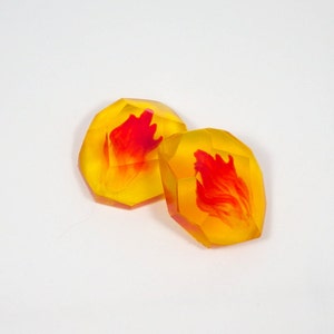 Peut inclure: Deux cabochons en résine jaune et orange avec des motifs de flammes rouges à l'intérieur.