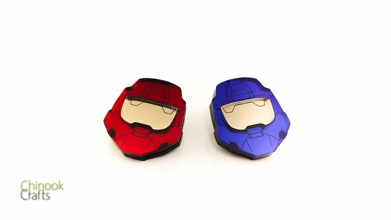 Pode incluir: Dois objetos em forma de capacete, um vermelho e outro azul, com viseira e design detalhado. Os capacetes s&atilde;o provavelmente inspirados em um videogame ou tema de fic&ccedil;&atilde;o cient&iacute;fica. Os objetos s&atilde;o exibidos em um fundo branco.