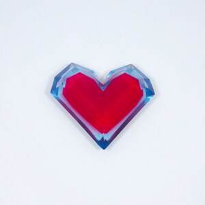 Pu&ograve; includere: Un fermacarte in resina a forma di cuore rosso con uno strato esterno blu e trasparente.