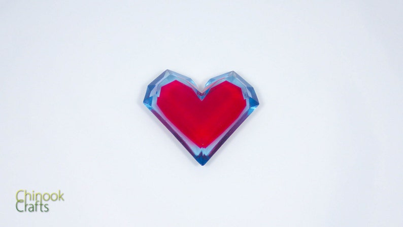 Pu&ograve; includere: Un fermacarte in resina a forma di cuore rosso con uno strato esterno blu e trasparente.