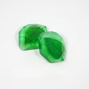 Puede incluir: Dos barras de jabón transparentes, facetadas y verdes con un diseño de hoja estampado en la parte delantera de cada barra.