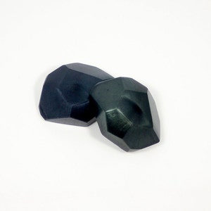 May include: Two dark green geometric shaped buttons. The buttons are made of a smooth, polished material.