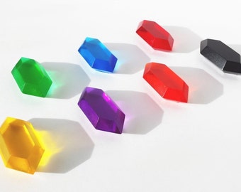 May include: Seven colorful plastic gems in the shape of a hexagon. The gems are arranged in a row from left to right: yellow, green, blue, purple, red, red, and black.
