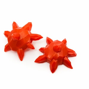 Puede incluir: Dos objetos de color naranja brillante, con forma de estrella, impresos en 3D, con una parte superior puntiaguda y múltiples facetas.