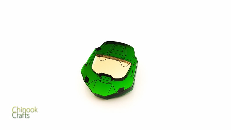 Pode incluir: Um objeto verde em forma de capacete angular com uma viseira dourada, que lembra um personagem de videogame. O objeto est&aacute; sobre um fundo branco, com o texto "Chinook Crafts" no canto inferior esquerdo.