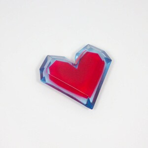 Pu&ograve; includere: Un fermacarte in resina a forma di cuore rosso con uno strato esterno blu e trasparente.