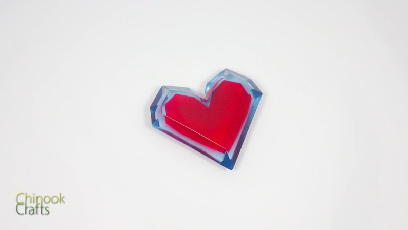 Pu&ograve; includere: Un fermacarte in resina a forma di cuore rosso con uno strato esterno blu e trasparente.