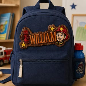 May include: A navy blue backpack featuring an embroidered patch with the name WILLIAM in orange letters, a red fire hydrant, yellow stars, and a cartoon firefighter character wearing a red helmet. A blue water bottle sits in the side mesh pocket.