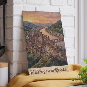 Könnte beinhalten: Ein rechteckiger Druck mit einer Landschaftsillustration von Heidelberg, Deutschland, gesehen vom Königstuhl aus. Das Kunstwerk zeigt einen Fluss, eine Steinbrücke und eine historische Stadt mit roten Dächern, beschriftet mit Heidelberg from the Königstuhl.