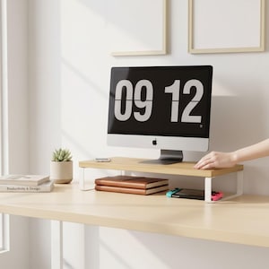 Peut inclure: Un support d'écran en bois clair avec des pieds en métal blanc soutient un écran d'ordinateur affichant l'heure 09:12. Une petite plante succulente dans un pot beige, des livres et un téléphone sont sur le bureau. Une main se tend vers l'écran.