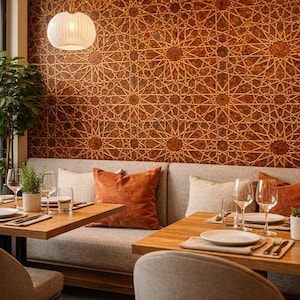 Op de afbeelding: Restaurantinterieur met houten tafels gedekt voor het diner. Grijze zitplaatsen met oranje kussens tegen een muur met een geometrisch patroon. Een hanglamp verlicht de scène. Glazen, borden en bestek zijn zichtbaar.