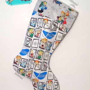 May include: A Christmas stocking featuring a pattern of The Jetsons cartoon characters in a retro style. The stocking has a gray background with images of the characters in a grid pattern. The top of the stocking has a gray background with images of the characters.