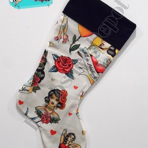 May include: A white Christmas stocking with a black velvet cuff. The stocking is decorated with a repeated pattern of colorful tattoos, including roses, hearts, and pin-up girls. The text "All or Nothing" is visible on the stocking.