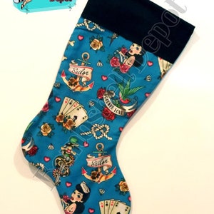 May include: A blue Christmas stocking with a black cuff, featuring a nautical tattoo design. The pattern includes anchors, roses, playing cards, sailor pin-up girls, and the words "Forever Love" and "Sailor".