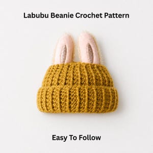May include: Mustard yellow crochet beanie with bunny ears. The ears are pink with glitter accents and a soft, fuzzy texture. The text "Labubu Beanie Crochet Pattern" and "Easy To Follow" are displayed on the image.