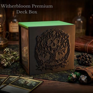 May include: A black deck box with a green top and a detailed skull and tree design. The box is labeled "Witherbloom Premium Deck Box". Several cards and dice are visible, suggesting a card game theme.