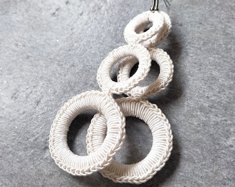May include: White crocheted earrings with multiple interlocking circles. The earrings are made of a thick, white cord and have a silver hook.
