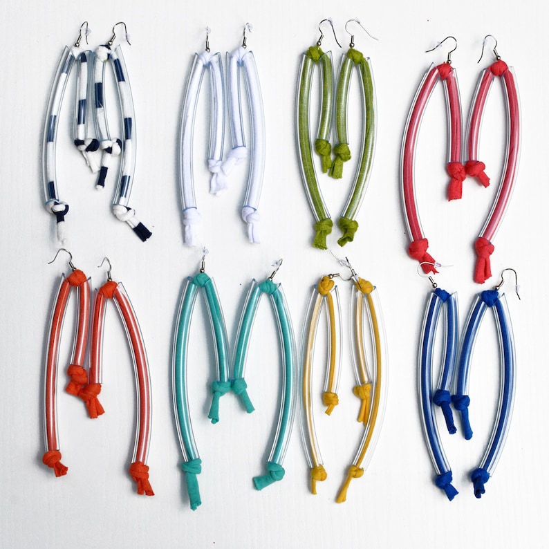 Peut inclure: Dix paires de boucles d'oreilles faites &agrave; la main avec des tubes en plastique transparent et des accents en tissu color&eacute;. Les boucles d'oreilles sont dispos&eacute;es en deux rang&eacute;es de cinq paires. Les couleurs comprennent le rouge, le bleu, le vert, le jaune et le blanc.