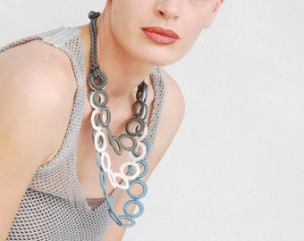 May include: A woman wearing a gray crochet top with a layered necklace made of white, gray, and blue crocheted circles.