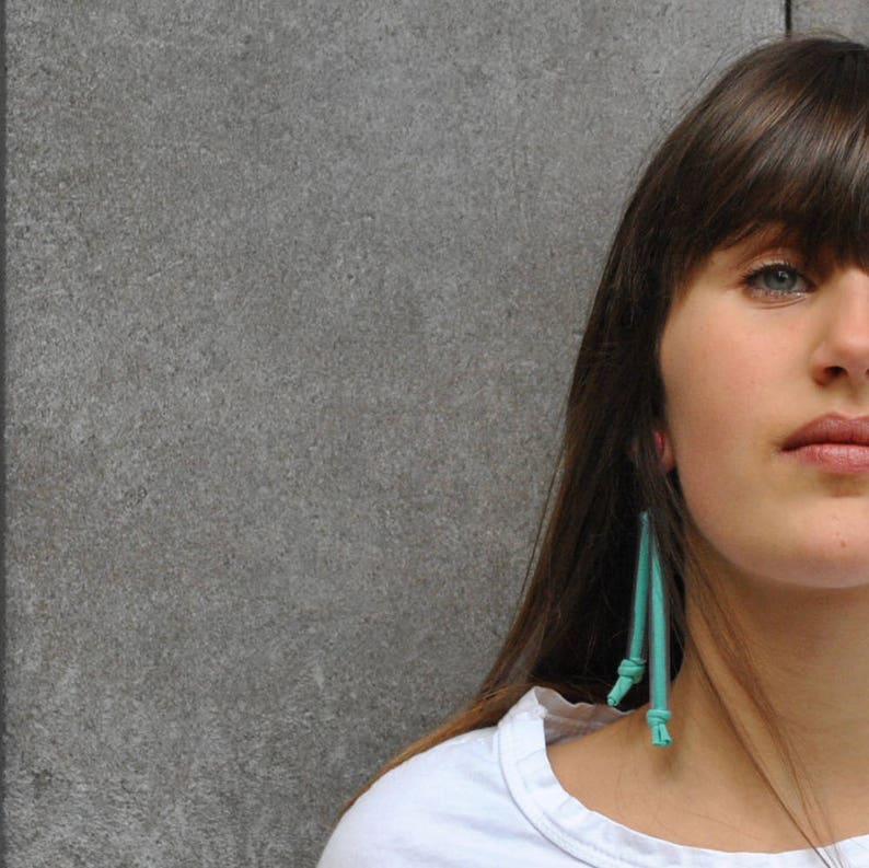 Peut inclure: Une femme aux longs cheveux bruns portant une chemise blanche et des boucles d'oreilles turquoise. Les boucles d'oreilles sont longues et pendent de ses oreilles.